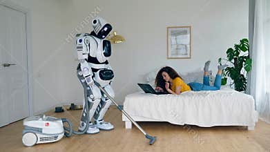 Girl works with a laptop while a cyborg vacuum cleans. Robot and human cooperation.