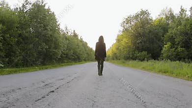 Caucasian guy in a black cardigan with a hood is in the middle of a country road with asphalt pavement surrounded by