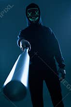 Anonymous criminal man with baseball bat in a black hoodie and neon mask