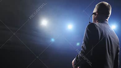 Rear view of men speaking through a microphone in dark conference hall. Man talks into microphones at press conference