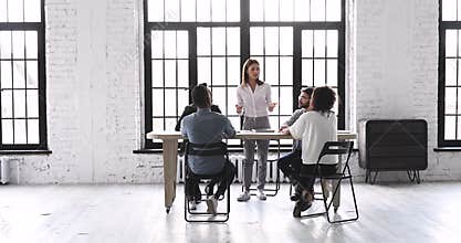 Female leader speaking at team briefing in modern office space