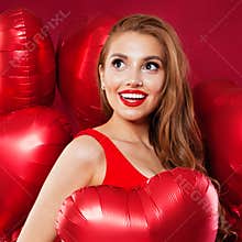 Pretty surprised woman smiling, looking up and holding red balloons