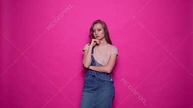 Beautiful serious young woman is thinking and thoughtful on pink background.