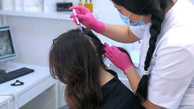 Doctor trichologist making injections mesotherapy in woman scalp in clinic.