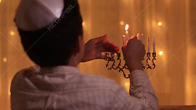 Rear view jewish boy lights fifth menorah candle during jewish holiday Hanukkah