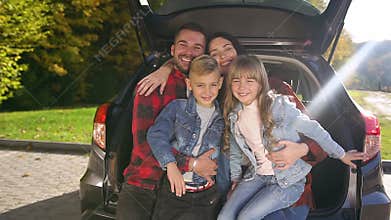 Close up of lovely cheerful trendy family which sitting in the trunk and posing on camera with sincerely smiles