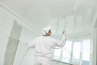 Painter worker with airless painting sprayer covering ceiling surface into white