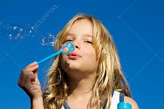Girl blows bubbles against blue sky