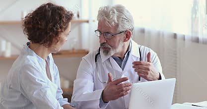 Old doctor consulting female patient showing test results on laptop