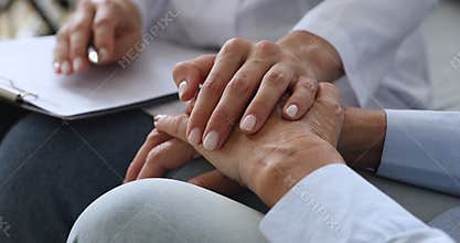 Empathic young nurse holding hand supporting elderly patient.