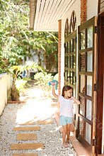 Little barefoot girl standing near door and playing with toy outside.