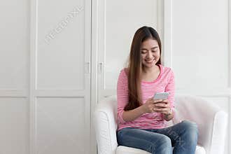 Beautiful young of Asian girl using a smartphone while sitting on the sofa in the living room at home, Asia women happy smile