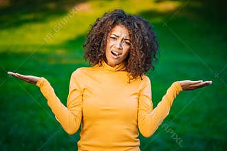 Unsure african american woman shrugs her arms, makes gesture of I don`t know, care, can`t help anything . Mixed race