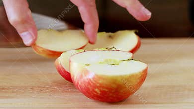 Man cuts red apple with kitchen knife on wooden board