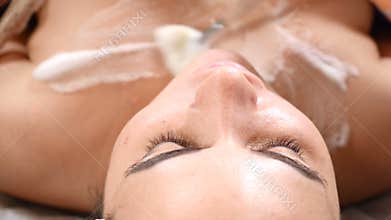 Beauty clinic. Young woman getting professional facial procedure. Beautician spreads foam mask on female face with brush