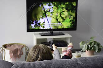 Young woman watching television with subtitles while sitting comfortably on sofa at home in living room