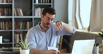 Ill male worker sitting at workplace blowing nose in tissue