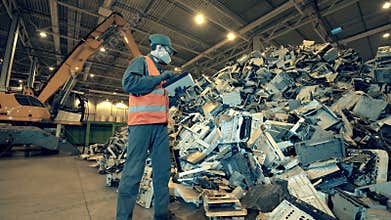 Dumpsite employee is observing a pile of broken electronic devices. Garbage, trash, waste recycling factory.