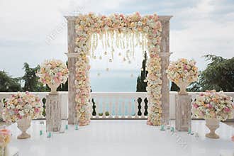 Elegant wedding arch with fresh flowers, vases on background of ocean and blue sky.