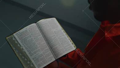 Prisoner in orange uniform reads bible in prison cell