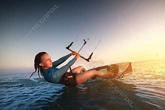Girl kitesurfing in a sexy hydrosuit with a kite in the sky on board in the blue sea, riding on the water waves