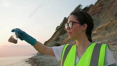 Scientist ecologist wearing protective gloves, vest and eyeglasses, examines sample flask of dirty water. Concept of