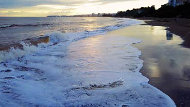 Drone views rolling waves onto beach at seaside town sunset. Beach scene at sunset, drone captures serene waves. Beach