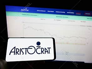 Person holding mobile phone with logo of gambling company Aristocrat Leisure Limited on screen in front of web page.