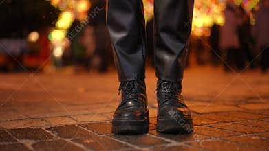 Legs of slim young woman in leather pants and boots dancing in slow motion on pavement in night city. Unrecognizable