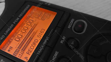 Finger presses record button of digital voice audio dictophone during interview or interrogation. Screen with wave form