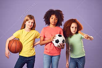 Studio Shot Of Children With Sports Equipment For Soccer Basketball Baseball On Purple Background