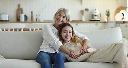 Adolescent daughter resting on couch with middle-aged attractive mother