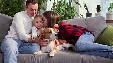 Happy family cuddling their dog beagle, having fun together in living room. Concept of pets, parenthood, love for