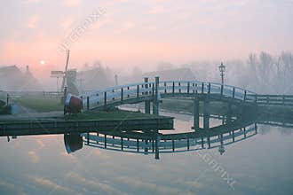Sun rises behind a bridge and a windmill