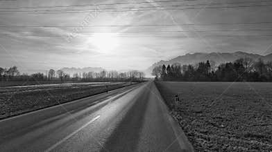Highway in winter landscape with mountains in background in black and white