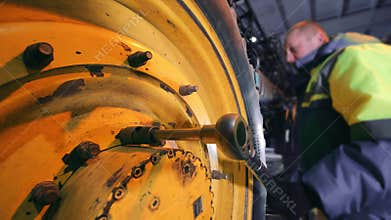 Maintenance of large-sized equipment. The master tightens the tractor wheel nuts.