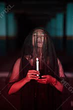 an Asian woman with closed eyes and a transparent veil stained with blood holds a candle in her hand during satanic worship