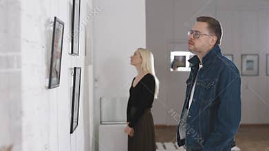 In an art gallery, at an exhibition of abstract paintings. A man and a woman are discussing objects of contemporary art