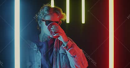 Portrait of young man drinking alcohol and dancing in night club with neon illumination