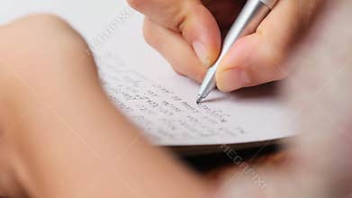 closeup of a hand journaling on a wooden table with the other hand blurry in the foreground