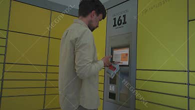Male customer using self-service automated delivery terminal to send package or storage locker to drop off parcel