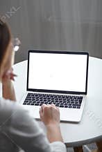 Mockup white screen laptop woman using computer while sitting at table at home, back view