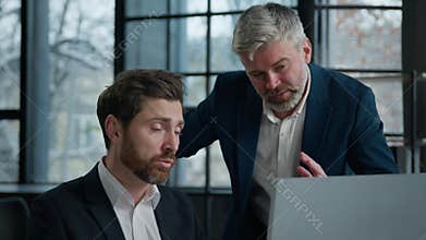 Two confused caucasian businessmen men partners colleagues talk arguing in office looking screen computer laptop