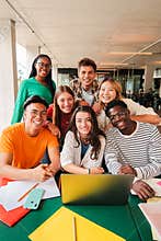 Vertical portrait. Group of young teenage students siting at library, using a laptop and looking at camera. Happy