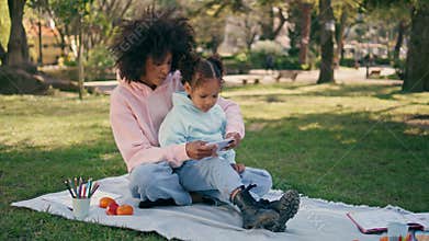 Mother daughter looking smartphone at picnic park. Mom showing cartoon to girl.