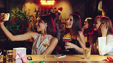 Elegant, beautiful young women, friends meeting in bar, restaurant, drinking cocktails, taking selfie. Christmas, winter