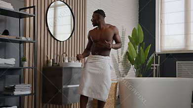 Funny happy ethnic man African American male muscular athletic guy good physical shape dancing with bath towel on hips