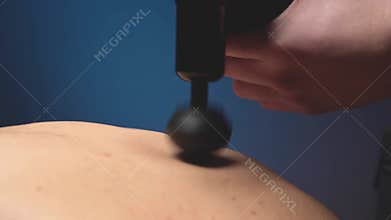 Close-up slow motion percussion shock wave massage using an electric massager. Massage the lower back of a male athlete