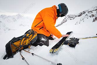 Ski tourist repairs skis in snowy mountains. Snow and winter activities, ski touring in the mountains