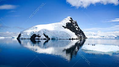 Antarctica, Lemaire Channel, snow covered mountain reflecting in sea. Penguins on ice floe in beautiful landscape.